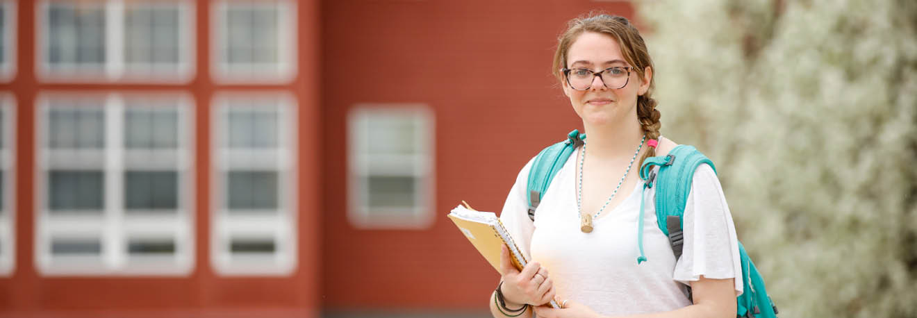 FLCC student with glasses and a backpack standing outside the main campus.