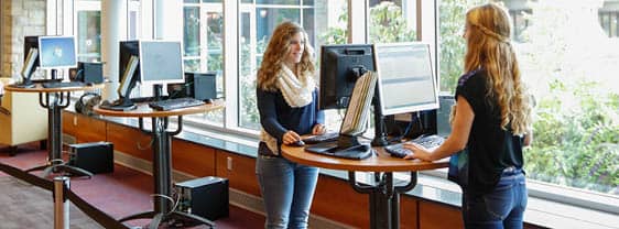 Two FLCC students standing at the One Stop Center self-service computer kiosks completing online forms.