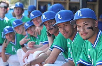 The men's baseball team sit in a dugout, ready for the game to start.