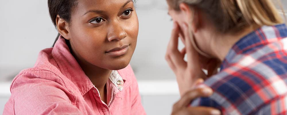 A chemical dependency counselor looks attentively at a woman in distress. She reaches out to gently touch the patient's shoulder.