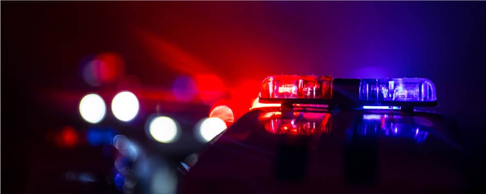 Red and blue police lights shine against a dark, blurred background at the scene of an accident.