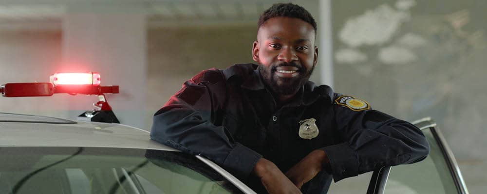 A police officer leans casually against the open door of his squad car, posing for a portrait.